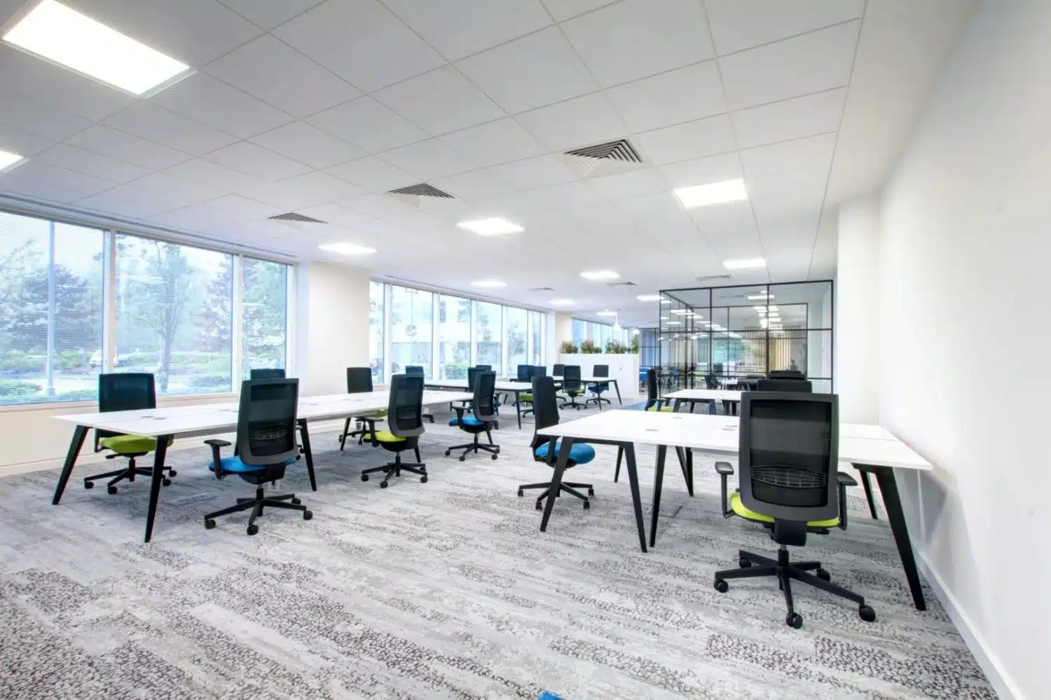 Modern office space with wooden cubicles, two people at a table, and a reflective ceiling featuring illuminated lines