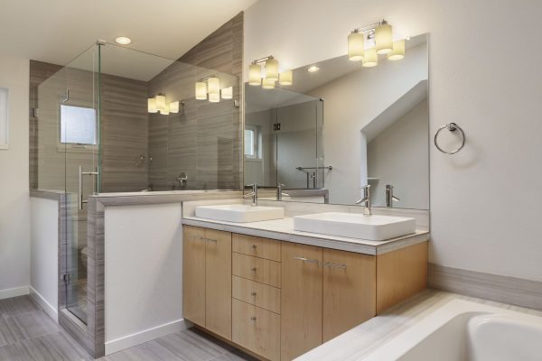Modern ensuite bathroom featuring dual sinks, glass shower, wooden cabinetry, and stylish lighting fixtures. Pro Renovations