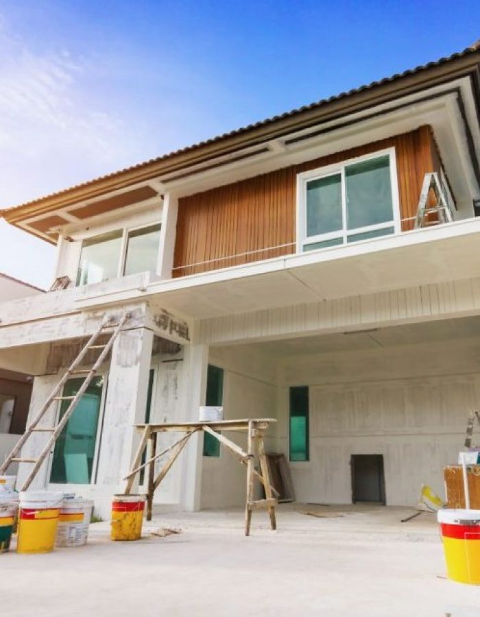 Renovated house exterior with scaffolding, ladders, and paint buckets, showcasing ongoing house renovations under a clear sky