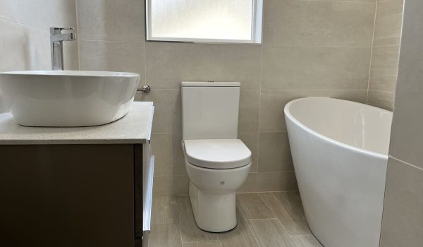 IMG_2339 Modern bathroom featuring a freestanding tub, wall-mounted sink, and sleek toilet against light tiled walls. Pro Renovations