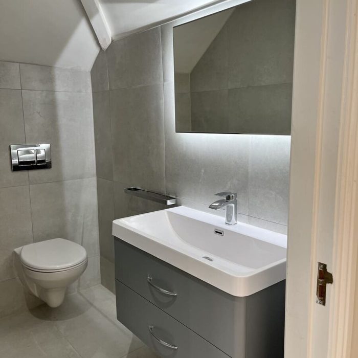 Modern bathroom featuring a wall-mounted sink, gray cabinetry, and a large mirror with soft lighting. Pro Renovations gallery