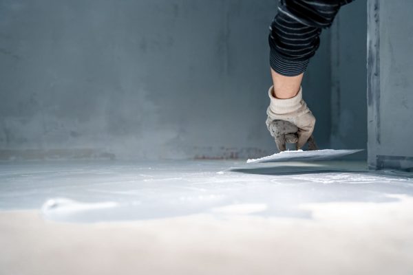 A gloved hand applies a smoothing tool to a wet surface in a gray-walled bathroom during residential bathroom renovations