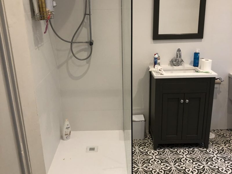 Modern walk-in shower with glass panel, gray patterned floor tiles, and a dark vanity with a mirror in a family bathroom reno