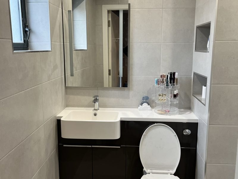 Modern bathroom with gray tiles, a white sink, dark cabinetry, a mirror, and a toilet, showcasing accessible design elements