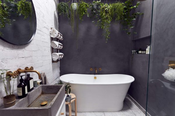 Stylish wet room with a freestanding bathtub, concrete sink, greenery, and elegant fixtures against a gray wall