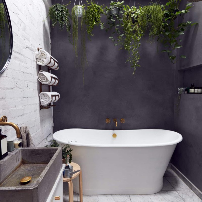 Stylish wet room with a freestanding bathtub, concrete sink, greenery, and elegant fixtures against a gray wall