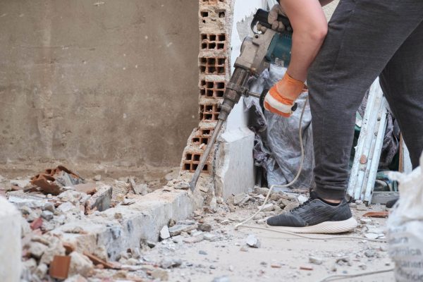A worker uses a power tool to break concrete in a bathroom renovation, surrounded by debris and construction materials