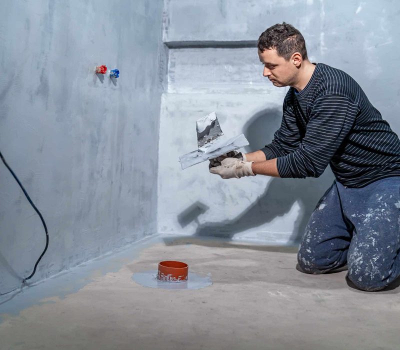 A man kneels on a bare floor, applying plaster to a wall in a family bathroom renovation project