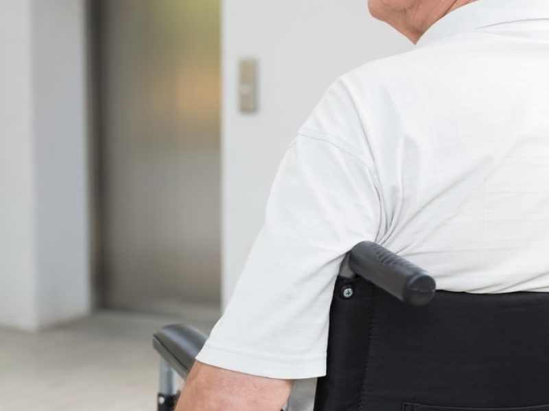 Elderly man in a wheelchair facing an elevator, highlighting accessibility challenges related to Mobility Aids Grant Limerick